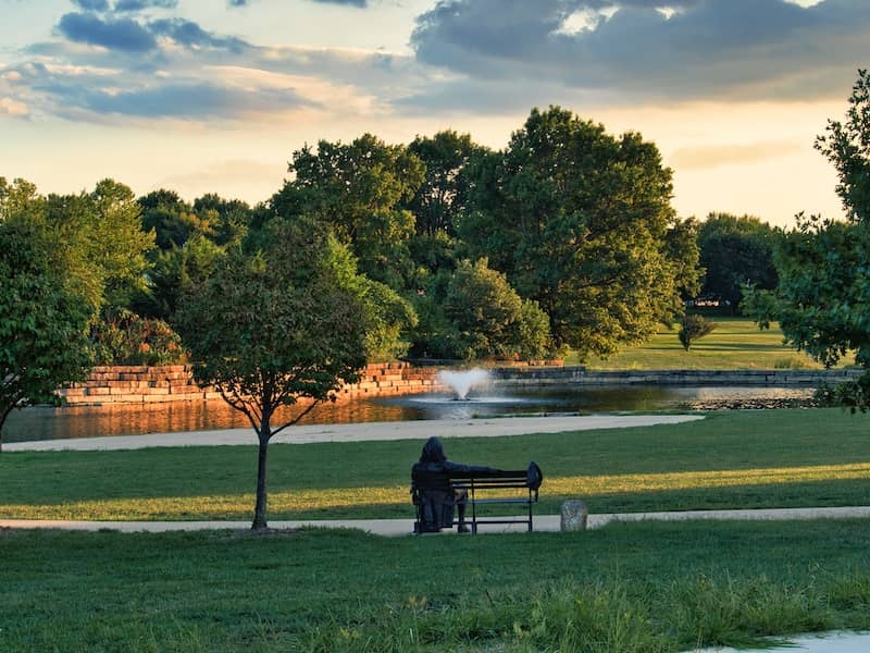 Pond with water fountain and statue surrounded by trees at the community center in Olathe, Kansas.